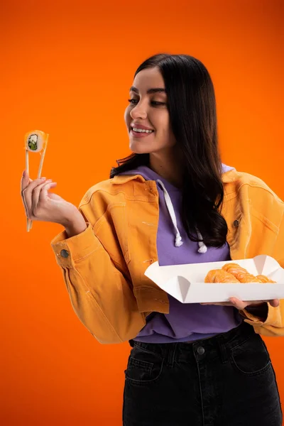 Stylish young woman looking at sushi and chopsticks isolated on orange — Stockfoto
