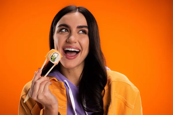 Portrait of excited woman holding sushi in chopsticks isolated on orange — Stock Photo