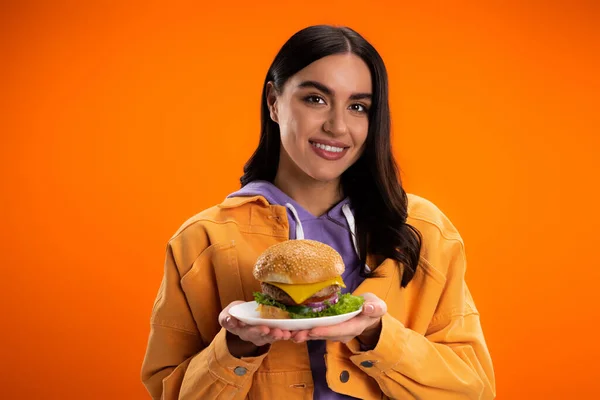Cheerful woman holding tasty burger with meat and cheese isolated on orange - foto de stock