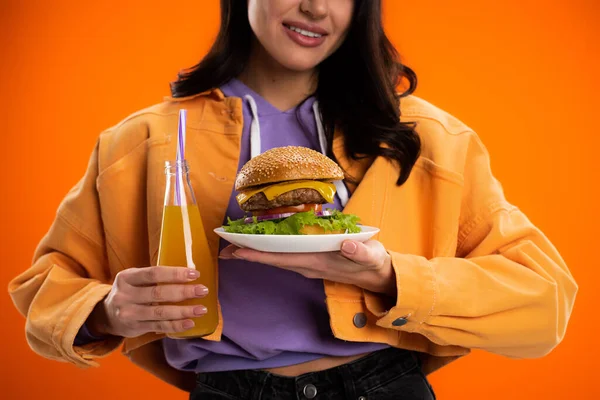 Partial view of smiling woman with tasty burger and fresh lemonade isolated on orange — Fotografia de Stock