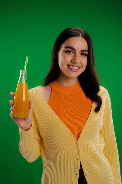 Happy brunette woman holding bottle of fresh juice with straw isolated on green — Photo de stock