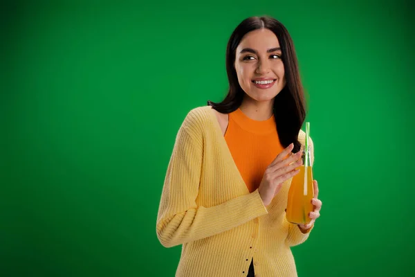 Stylish woman with bottle of fresh juice smiling and looking away isolated on green — Stock Photo