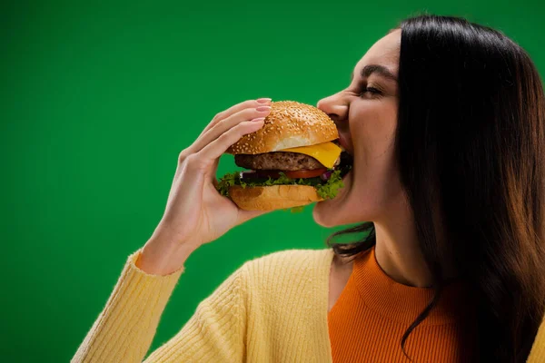 Hungry woman eating delicious burger isolated on green — Foto stock