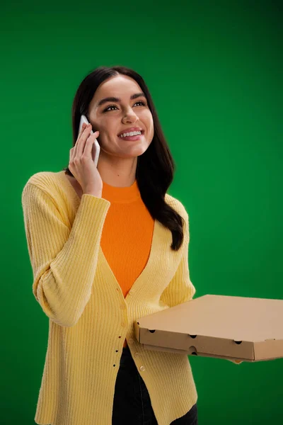 Happy young woman calling on smartphone while standing with pizza box isolated on green — Fotografia de Stock