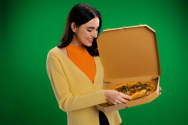Happy young woman holding carton box with delicious pizza isolated on green — Foto stock