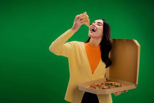 Young woman with open mouth holding carton box and delicious pizza isolated on green — Stock Photo