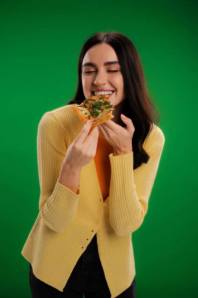 Pleased woman with closed eyes eating delicious pizza isolated on green — Photo de stock