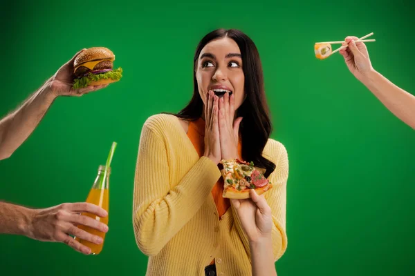 Изумленная женщина закрывает рот руками рядом с людьми, предлагая различные продукты питания изолированы на зеленый — стоковое фото