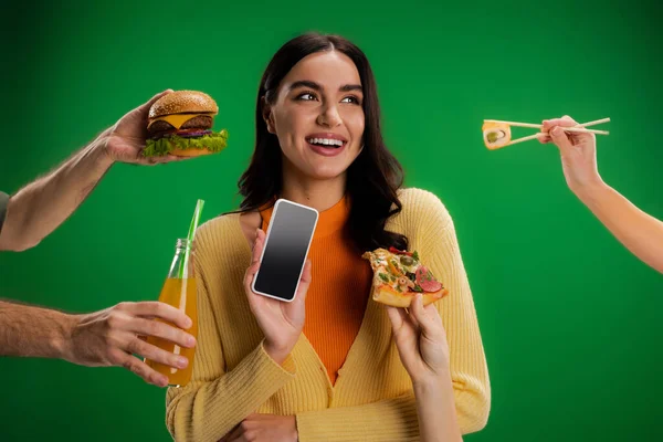 Mujer feliz sosteniendo teléfono inteligente con pantalla en blanco cerca de personas con surtido de alimentos aislados en verde - foto de stock