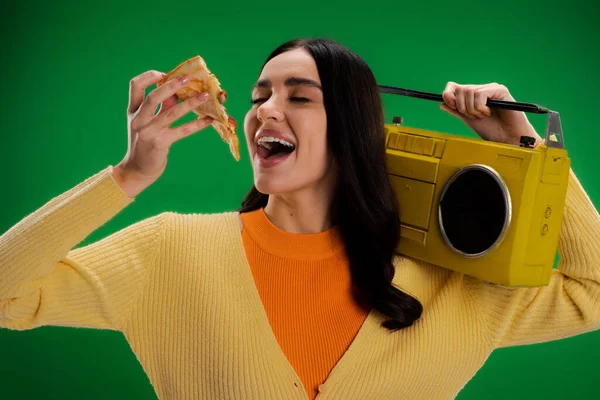 Hungry woman with boombox holding piece of pizza near open mouth isolated on green — Photo de stock