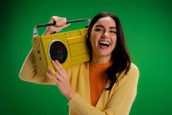 Excited brunette woman holding boombox and laughing at camera isolated on green — Photo de stock