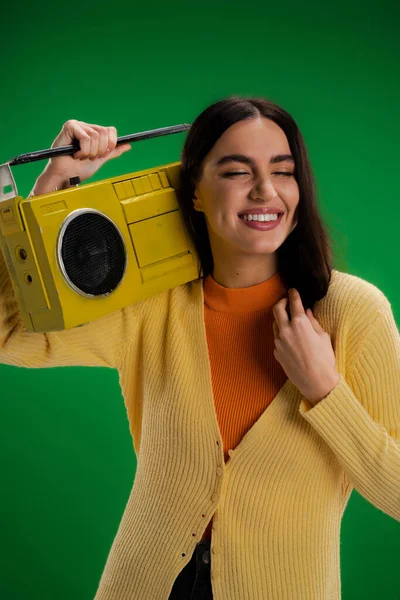 Cheerful woman with closed eyes holding vintage boombox isolated on green - foto de stock