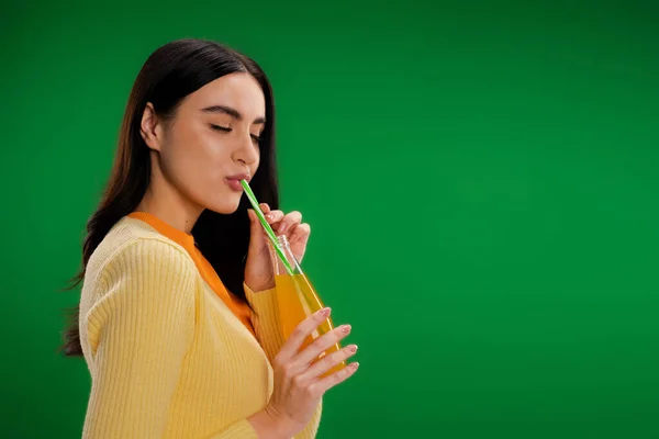 Brunette woman with closed eyes enjoying fresh lemonade isolated on green — Stock Photo