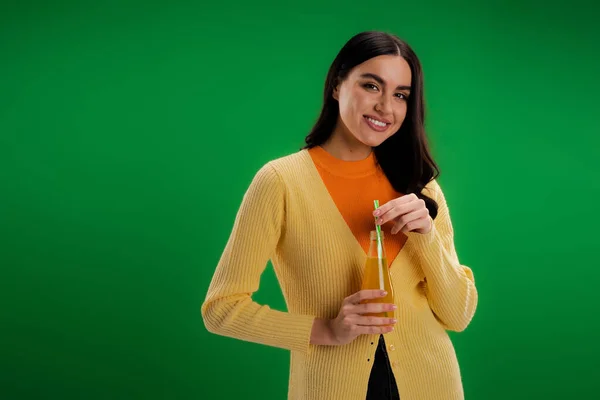 Young brunette woman with bottle of natural juice smiling at camera isolated on green — Stockfoto
