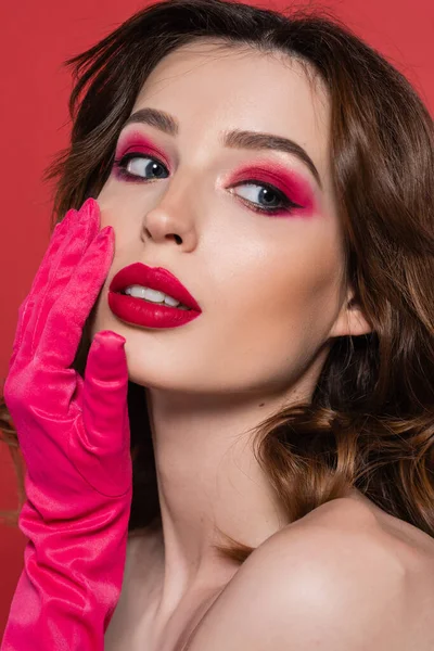 Portrait of young woman with magenta color eye shadow touching face with hand in glove isolated on pink — Photo de stock