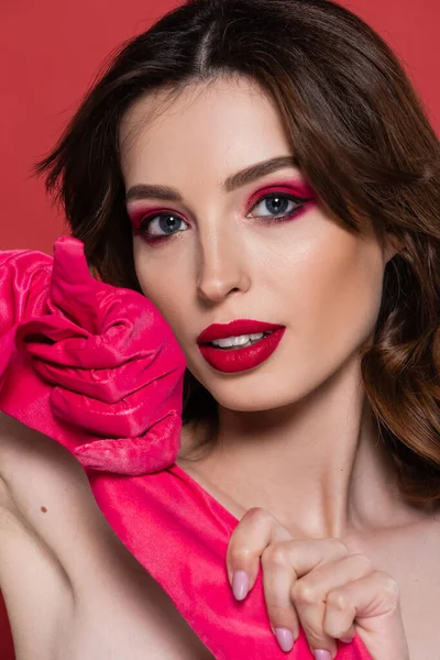 Portrait of young woman with magenta color eye shadow holding bright glove isolated on pink — Stockfoto