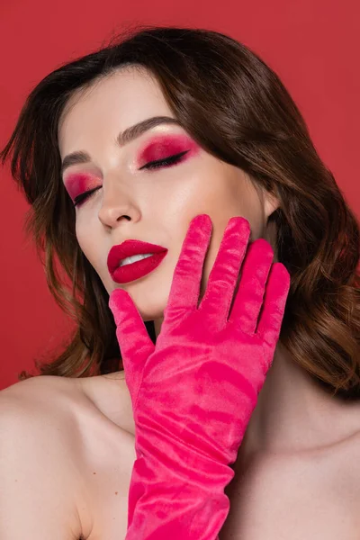 Портрет брюнетки з кольоровою рукавичкою пурпурового кольору, що торкається обличчя ізольовано на рожевому — стокове фото