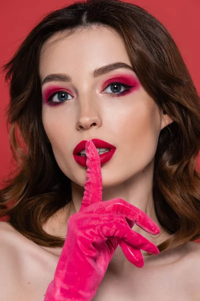 Portrait of young woman with magenta color eye shadow showing hush sign isolated on pink - foto de stock