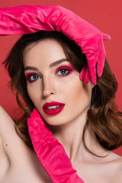 Portrait of young woman with magenta color eye makeup and gloves posing isolated on pink - foto de stock