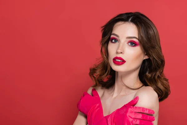 Young woman with magenta color makeup standing with crossed arms while embracing herself isolated on pink — Stock Photo