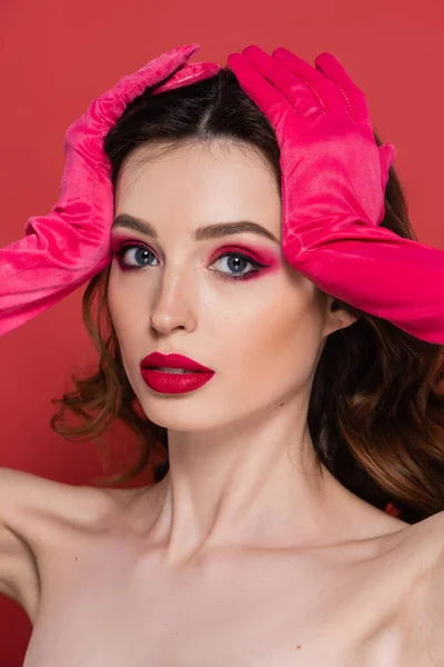 Portrait of young woman with magenta color eye makeup looking at camera while posing in gloves isolated on pink — Stock Photo
