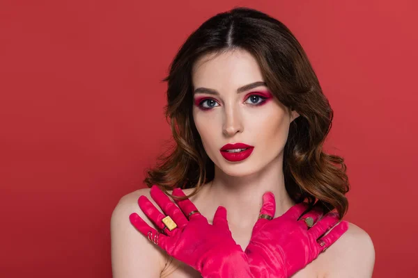 Portrait of young woman with magenta color gloves and golden rings posing with crossed arms isolated on pink — Stock Photo