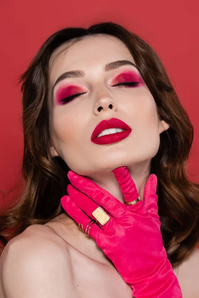 Portrait of young woman with magenta color glove with golden rings touching neck isolated on pink — Stockfoto