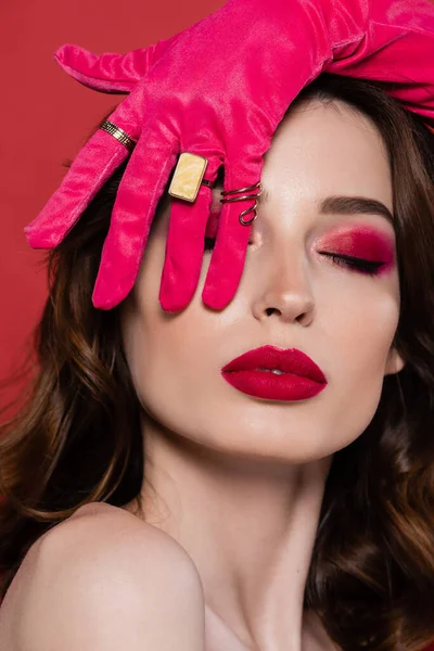 Brunette young woman in magenta color glove with golden rings covering eye isolated on pink — Stock Photo