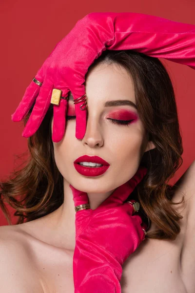 Portrait of young woman with magenta color makeup posing in gloves with golden rings isolated on pink — Photo de stock