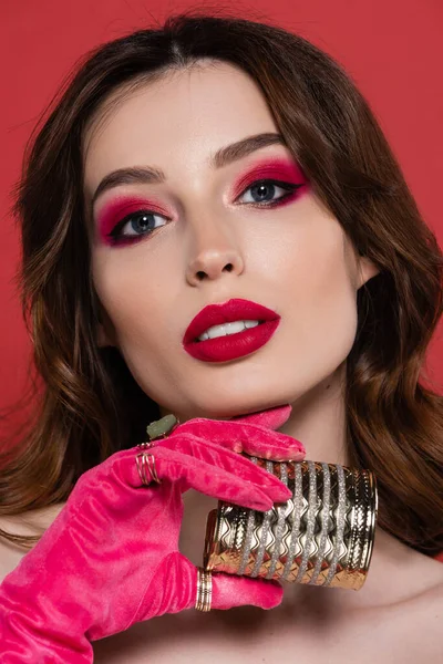 Portrait of young woman in magenta color glove with rings holding golden bracelet isolated on pink — Stock Photo