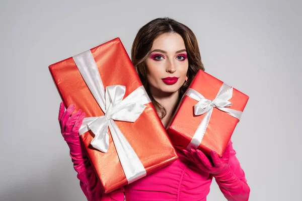 Brunette young woman in magenta color dress and gloves holding presents isolated on grey — Photo de stock