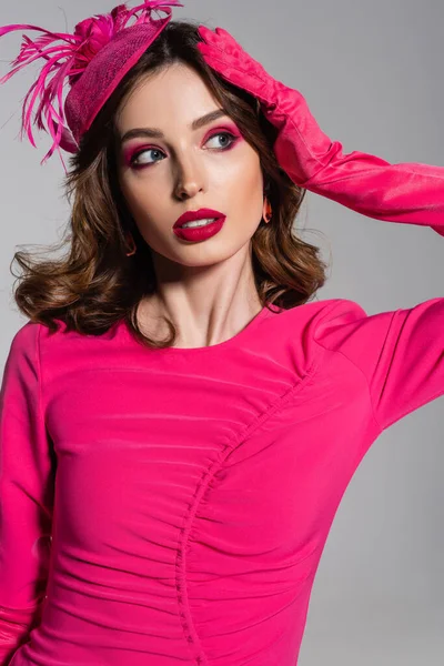 Pretty young woman in magenta color glove and hat with feather posing isolated on grey — Foto stock