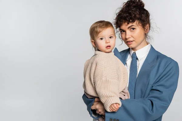 Successful businesswoman in blue suit holding in arms toddler daughter isolated on grey - foto de stock