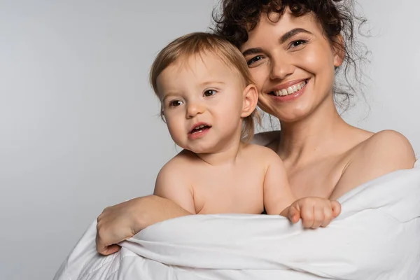 Mère souriante et tout-petit bébé fille recouvert de couette isolée sur gris — Photo de stock