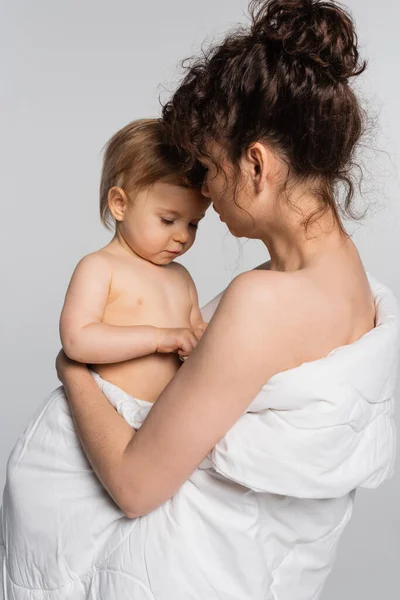 Кучерява мати тримає маленьку дівчинку, покриту ковдрою, ізольовано на сірому — стокове фото