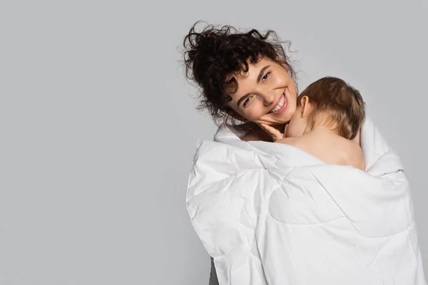 Happy mother and toddler daughter covered in white blanket isolated on grey — Photo de stock