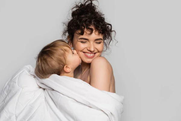 Tout-petit bébé fille baisers joue de heureux mère recouvert de couette blanche isolé sur gris — Photo de stock