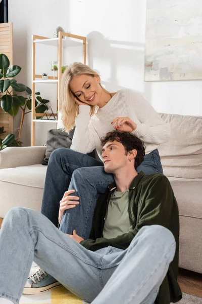 Young man hugging leg of happy girlfriend in living room — Foto stock
