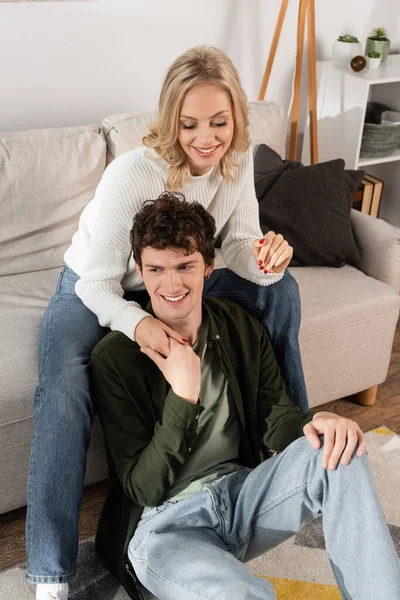 High angle view of happy blonde woman in white sweater hugging curly boyfriend in living room — Foto stock