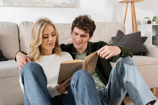 Young couple smiling while reading book together in living room — Stock Photo