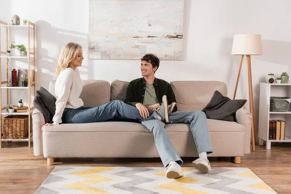 Full length of cheerful man in jeans looking at blonde girlfriend in living room — Stock Photo