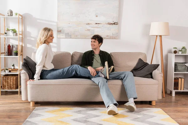 Full length of cheerful man in jeans looking at blonde girlfriend in living room — Foto stock