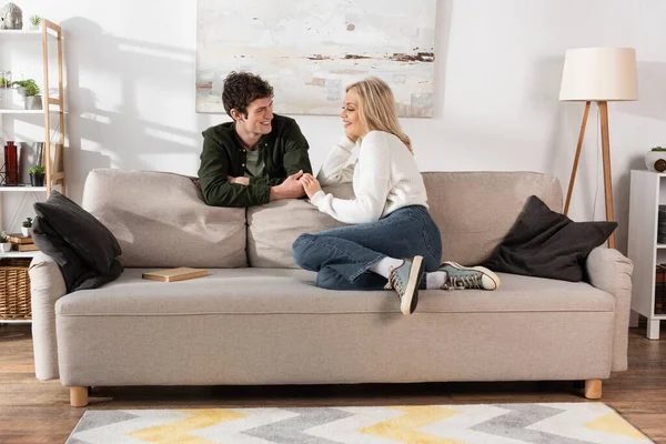 Full length of young woman with blonde hair looking at curly boyfriend in living room — Stock Photo