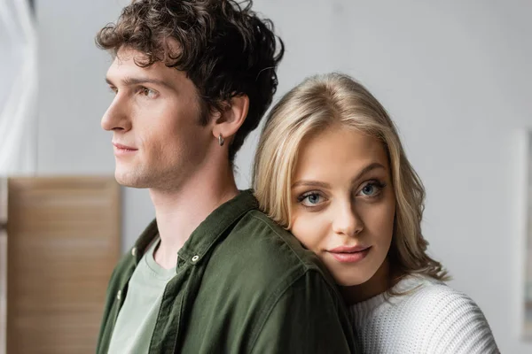 Portrait of blonde woman in white sweater leaning on back of curly young man — Stock Photo