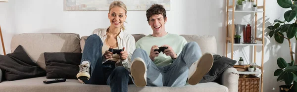 KYIV, UKRAINE - OCTOBER 24, 2022: excited young couple holding joysticks while playing video game, banner — Photo de stock