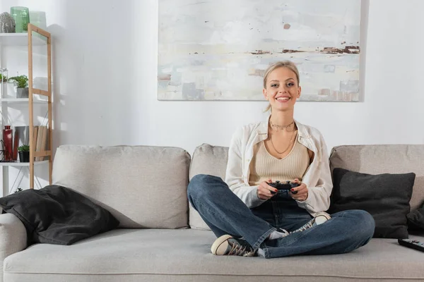 KYIV, UKRAINE - OCTOBER 24, 2022: cheerful young woman holding joystick while playing video game on couch — стокове фото