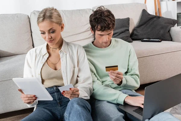 Молодий чоловік і жінка тримають гаджети і кредитні картки під час онлайн-покупки — стокове фото