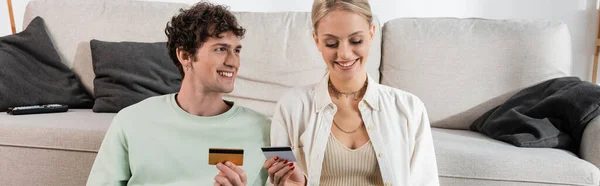 Веселий чоловік і щаслива жінка тримає кредитні картки у вітальні, банер — стокове фото