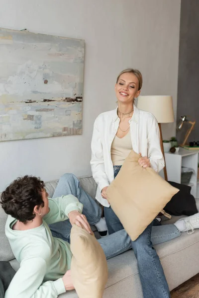 Cheerful woman having fun pillow fight with boyfriend in living room — Stock Photo