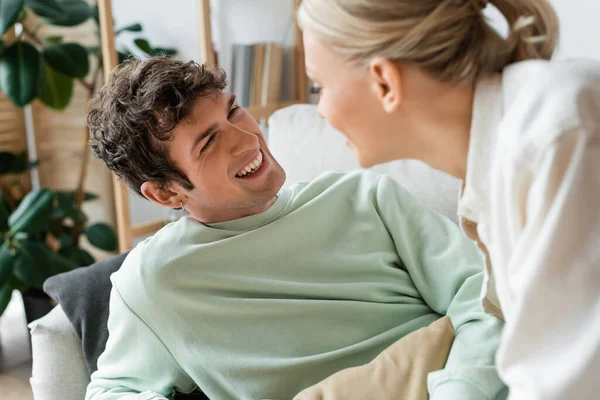 Cheerful young man laughing while looking at girlfriend on blurred foreground — стоковое фото